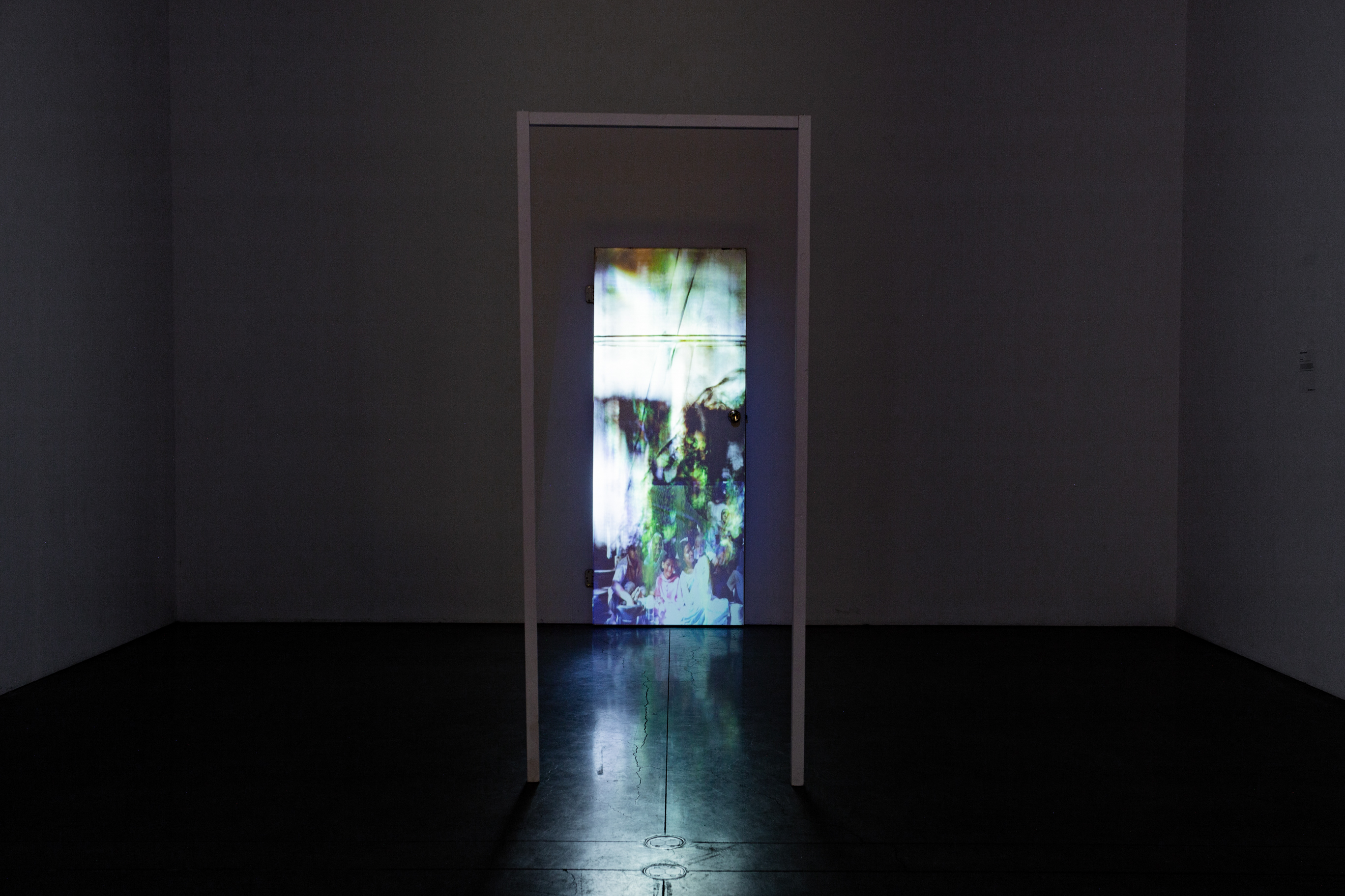 A narrow projection of a collage on a door in the center of a dark white room.